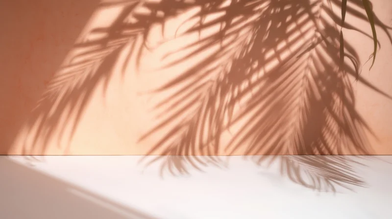 Palm leaf shadows cast on a peach wall and white floor in a minimalist interior