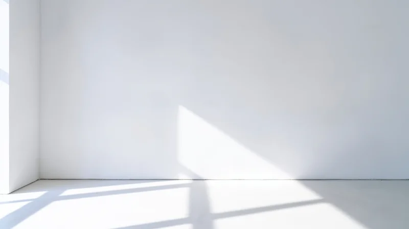 Empty white room corner with sunlight casting geometric shadows on floor and wall