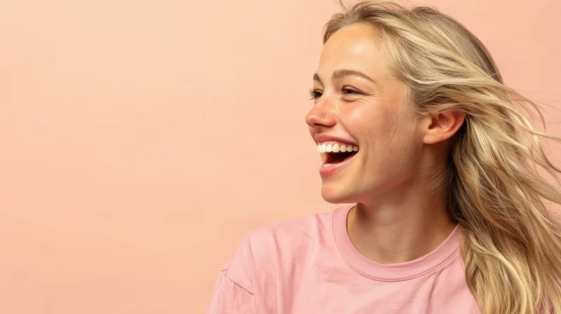 Young woman laughing with blonde hair in profile against a pink background wearing a pink tshirt