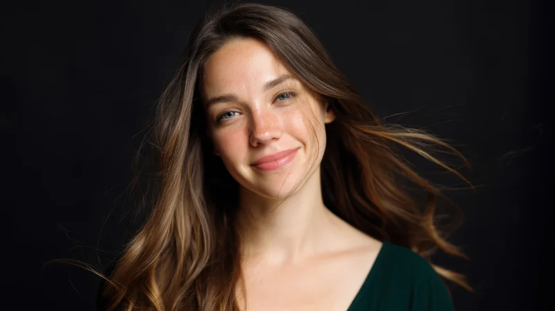 Young woman smiling with long brown hair flowing in soft light against dark background