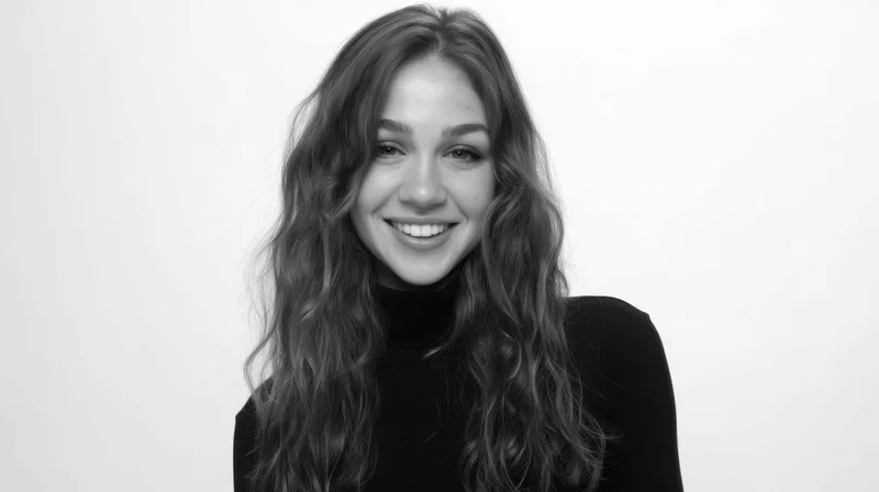 Smiling woman with long wavy hair in black turtleneck against white background