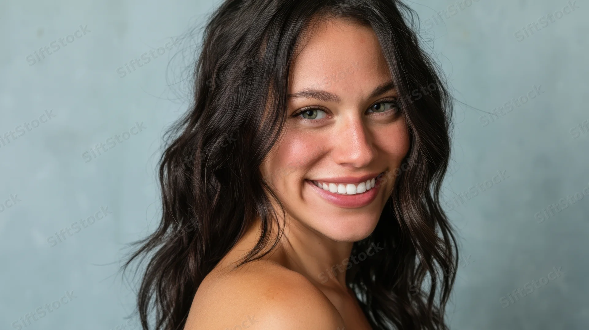 Young woman smiling with dark wavy hair in a studio portrait against a gray background