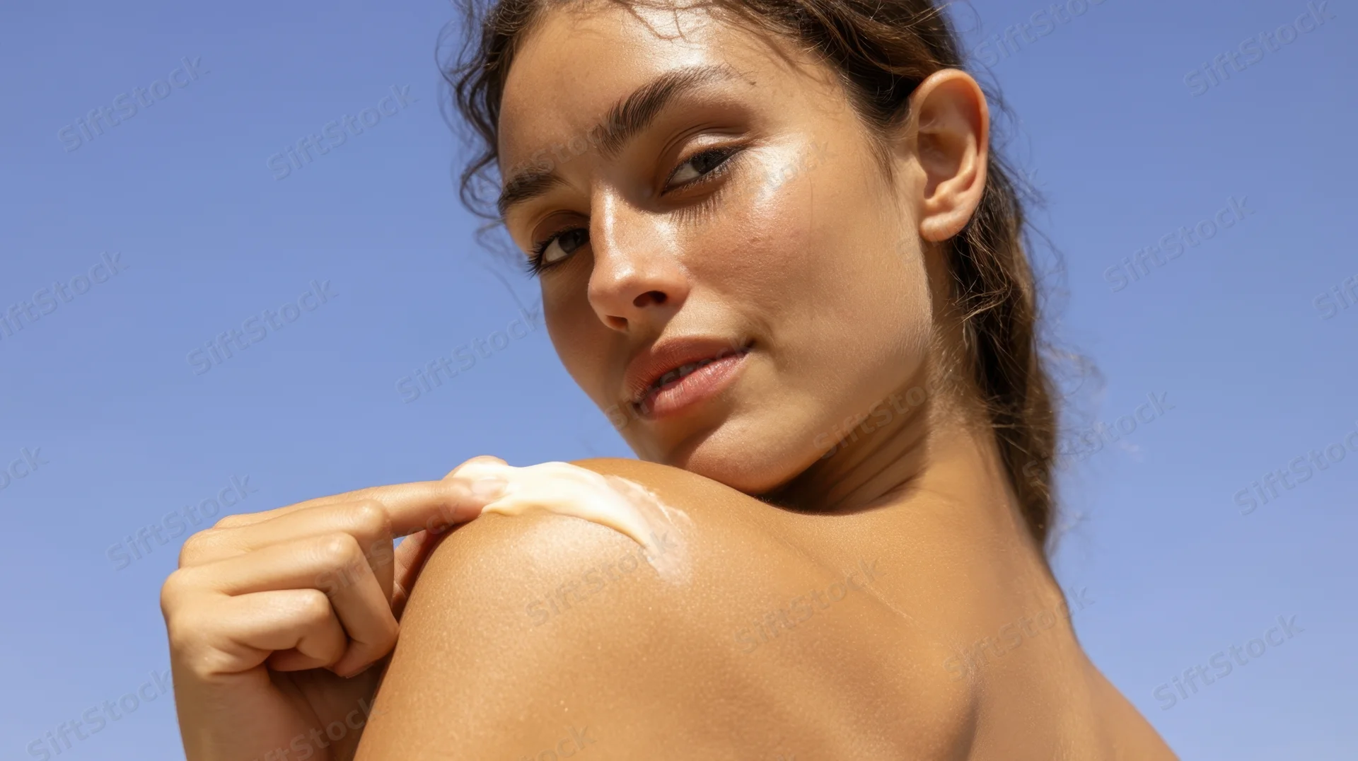 Young woman applying sunscreen to her shoulder outdoors under blue sky