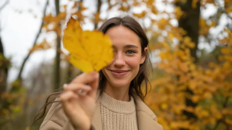 Young woman smiling while holding a yellow leaf in front of her face in an autumn forest