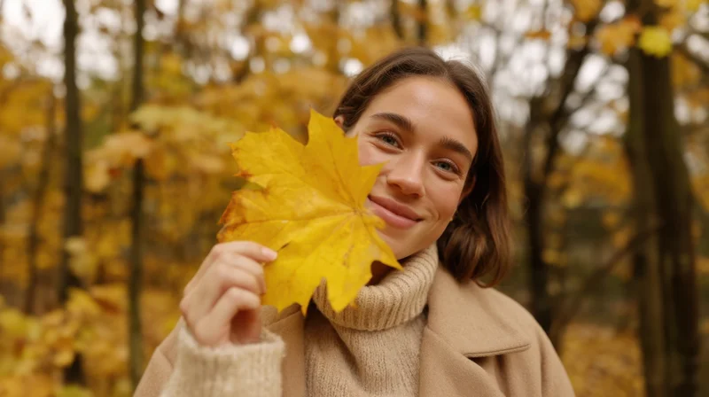 Young woman smiling with a yellow maple leaf in an autumn forest