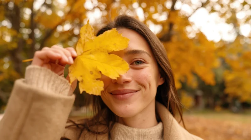 Young woman smiling with yellow autumn leaf covering one eye in park