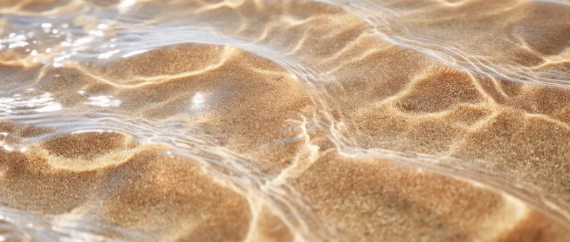 Rippling water over sandy beach surface under sunlight