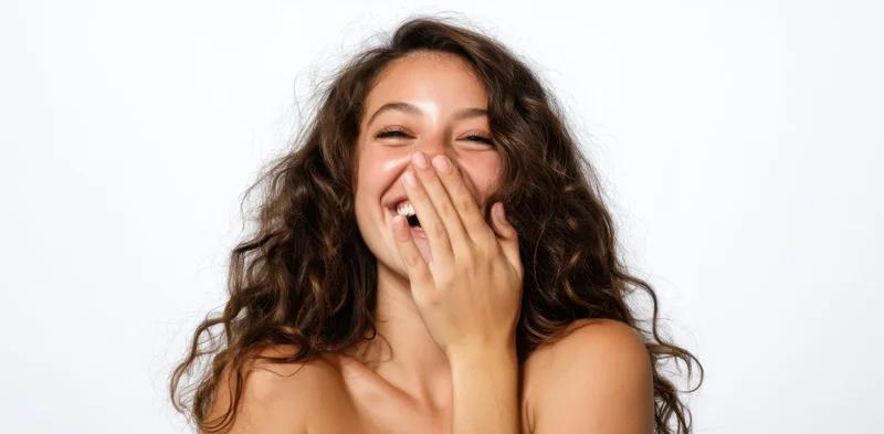 Young woman laughing with hand over mouth in studio portrait