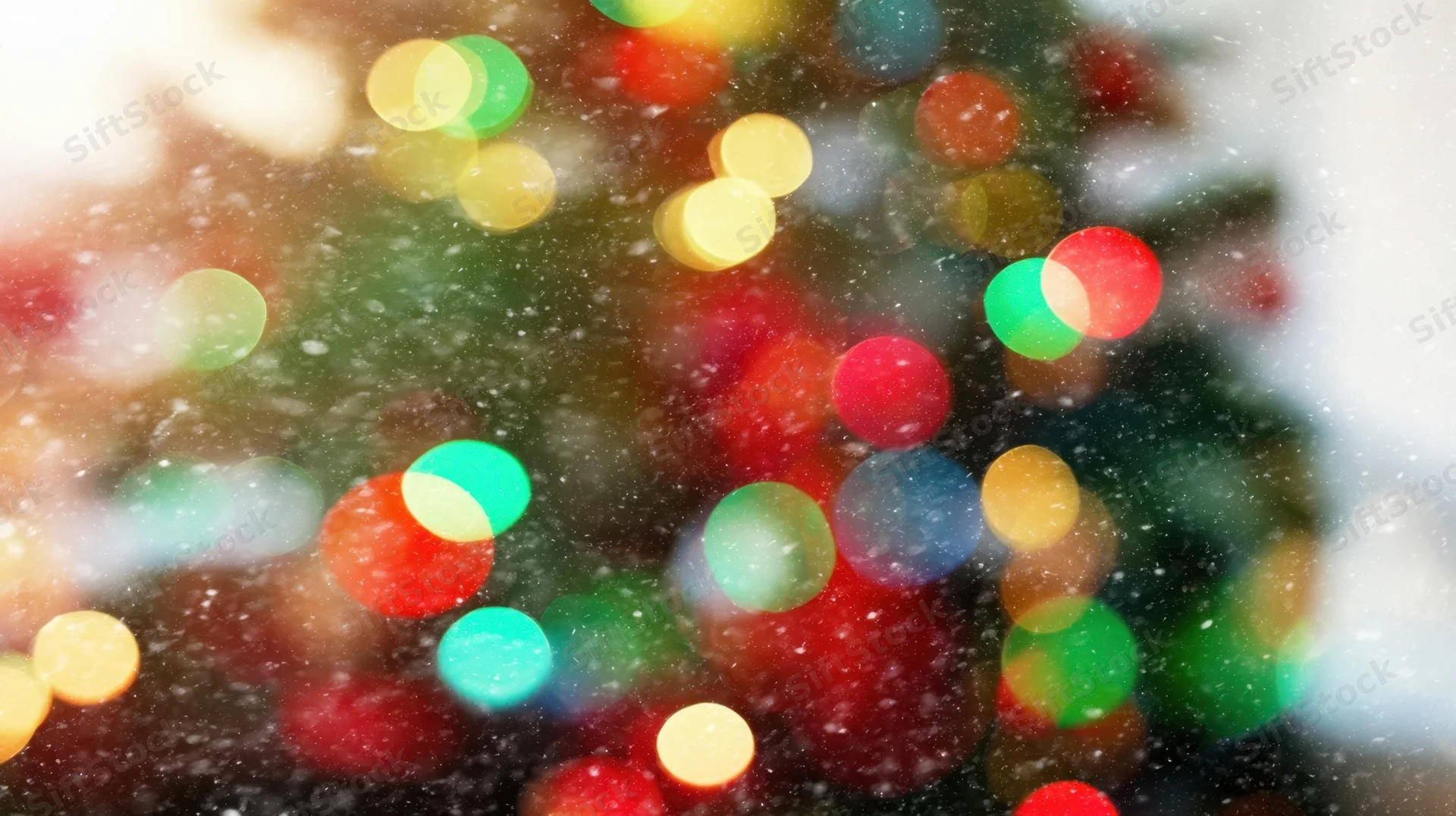 Blurred colorful christmas lights glowing through falling snow at night