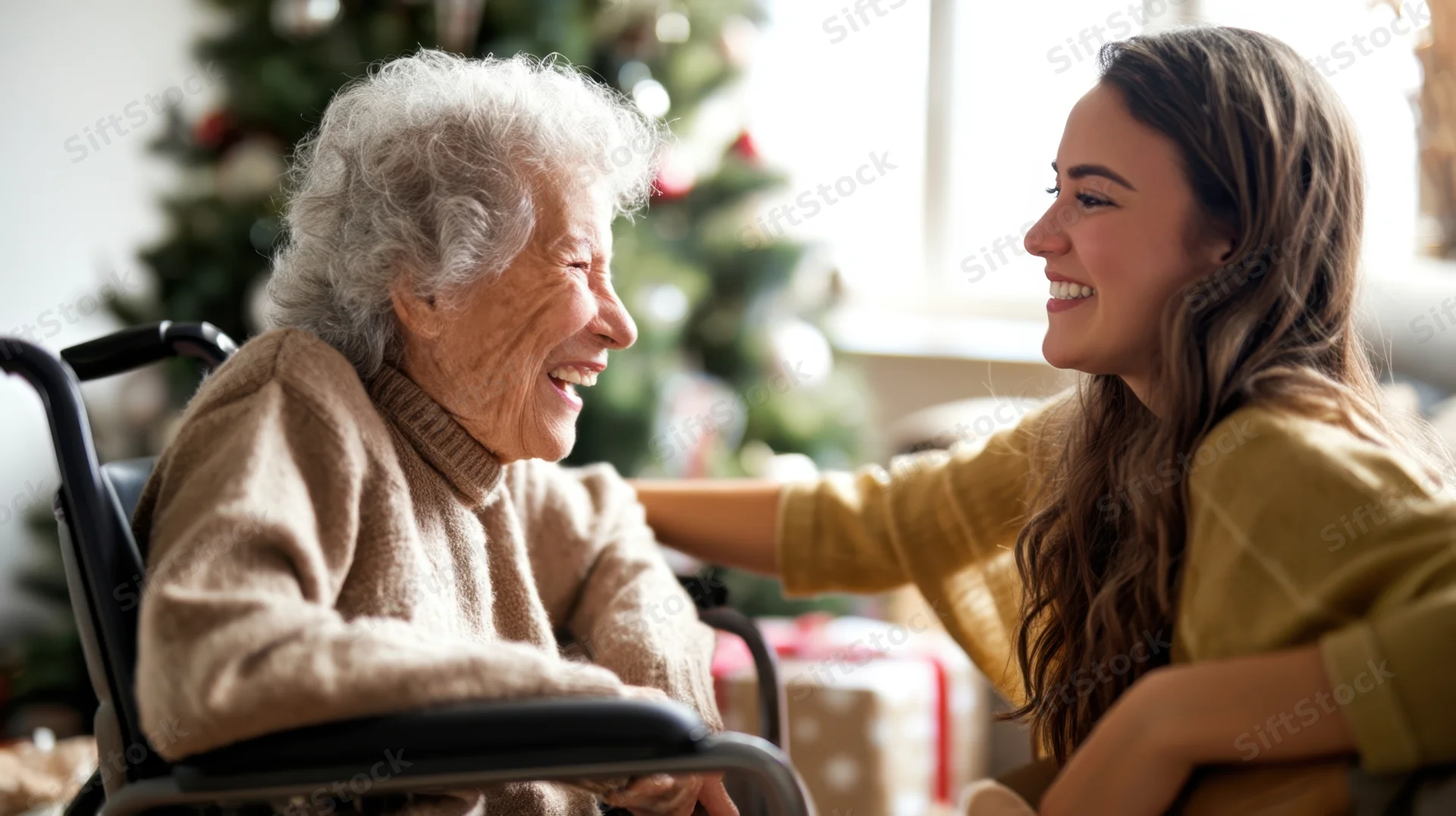 Senior woman in wheelchair smiling with young caregiver during christmas at home