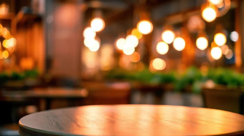 Round wooden table in a warmly lit cafe interior with blurred background lights and greenery