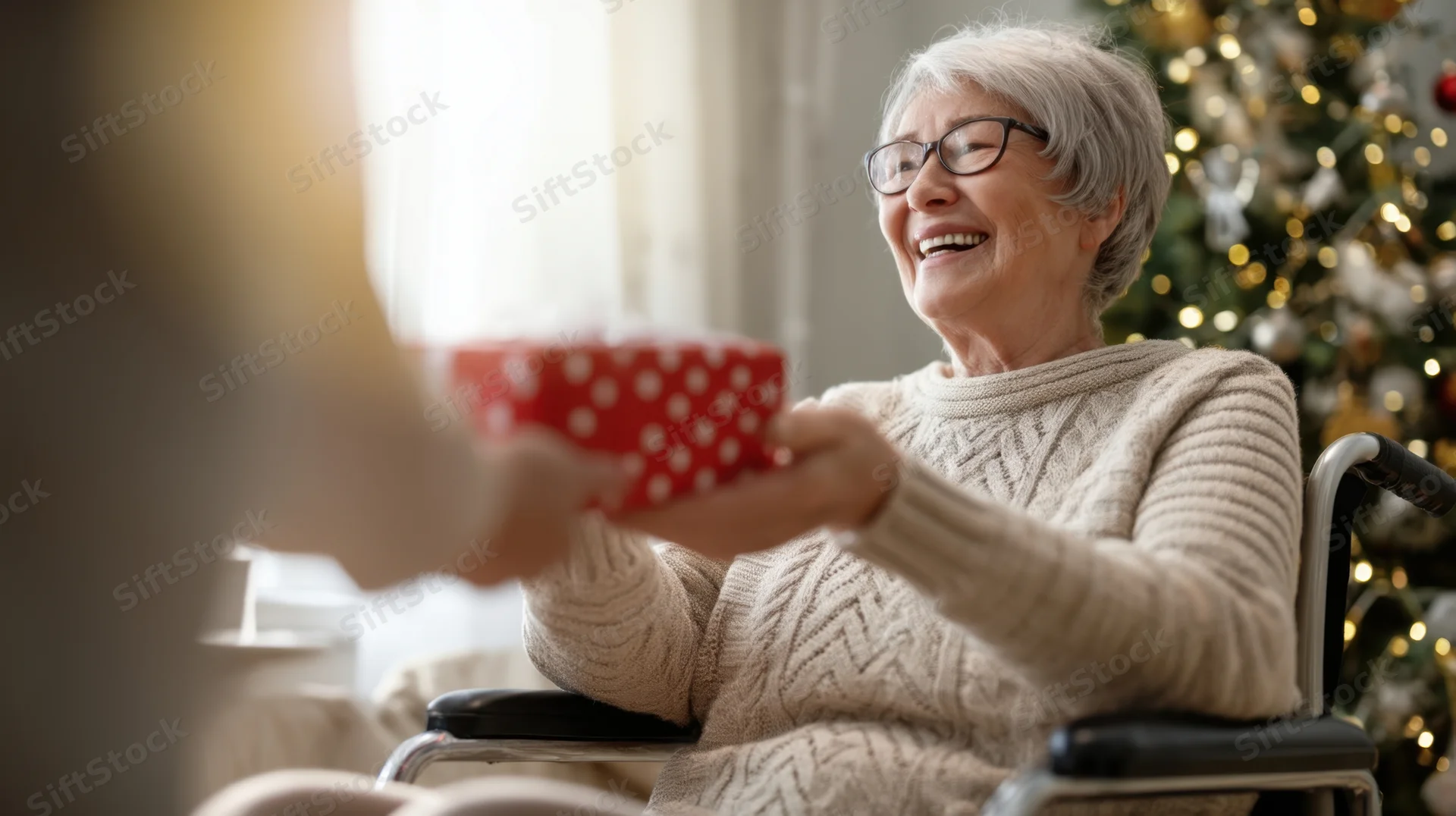 Senior woman in wheelchair smiling as she receives a wrapped gift near a decorated christmas tree indoors