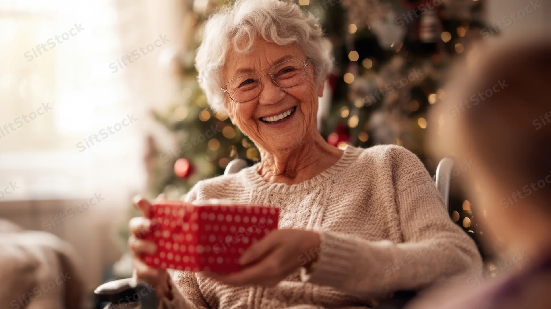 Elderly woman smiling while holding a wrapped gift in front of a decorated christmas tree at home