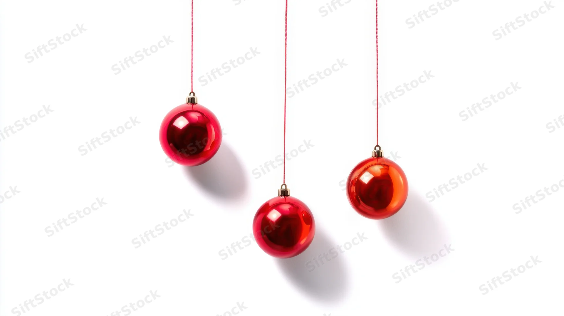 Three red glossy christmas ornaments hanging on strings against white background