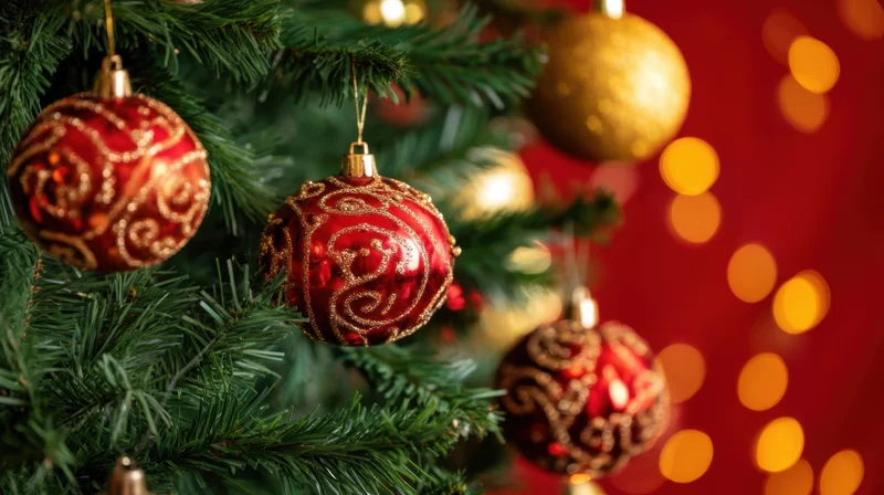 Red and gold ornaments hanging on a christmas tree with blurred lights in the background