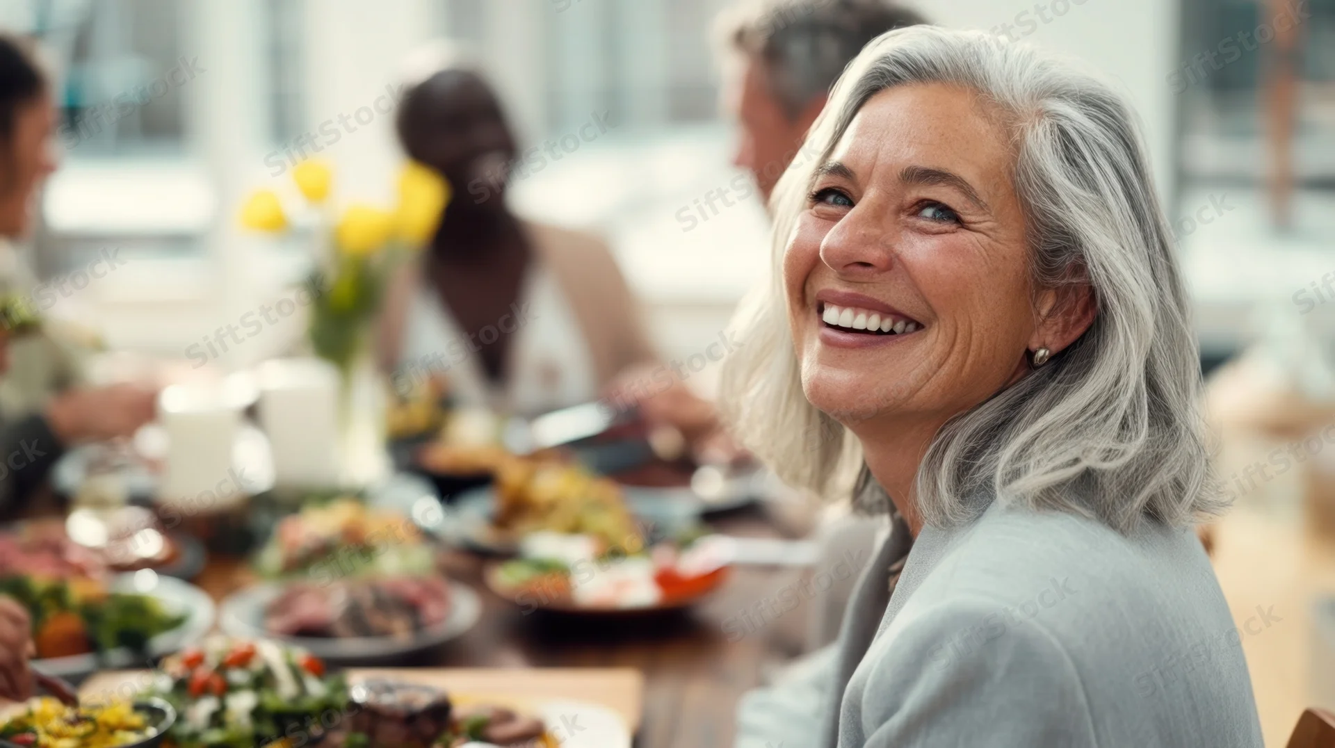 Smiling senior woman at a dinner table with diverse group enjoying a meal together indoors