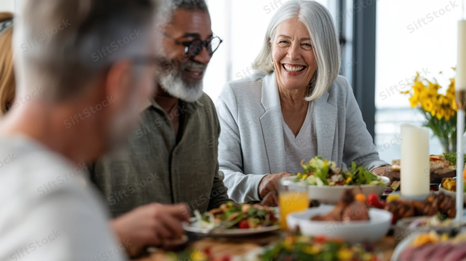 Smiling senior woman laughing during dinner with diverse group at dining table