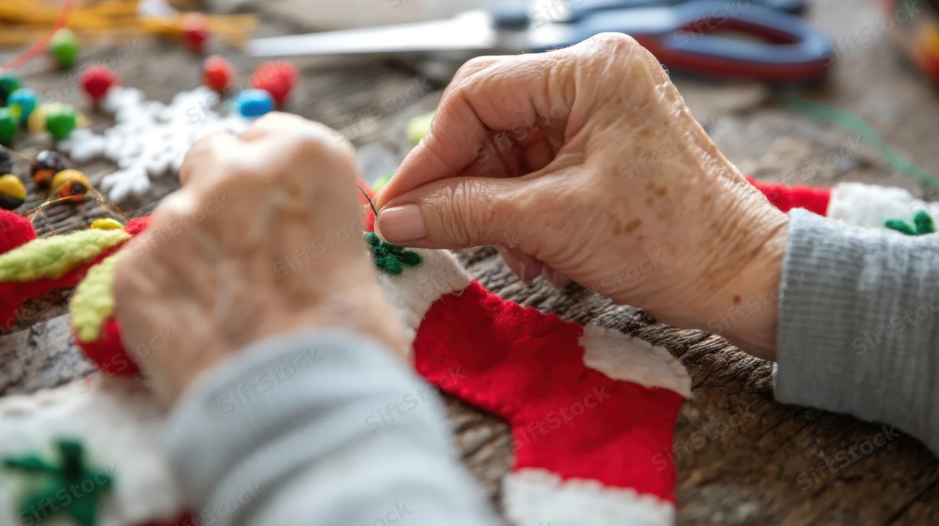 Elderly woman’s hands sewing felt christmas ornaments on a wooden table