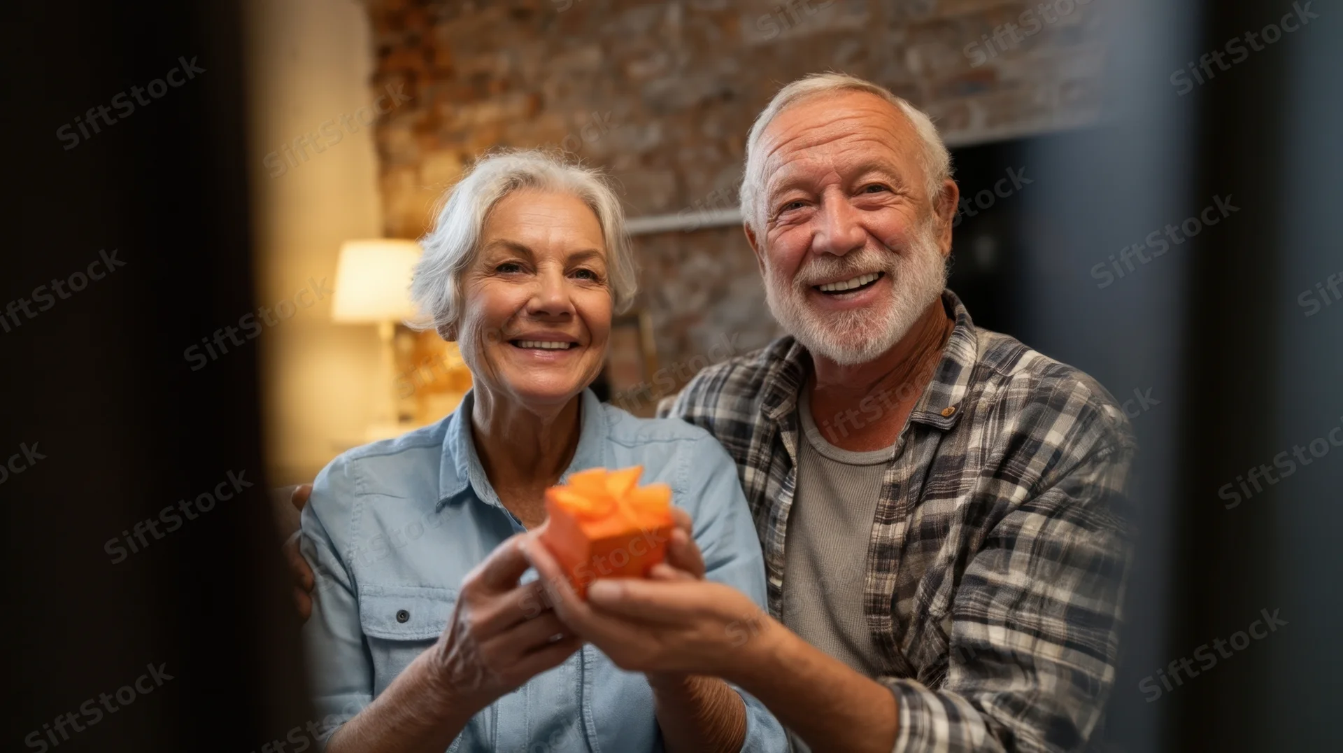 Elderly couple smiling and holding a small orange gift box in a cozy living room