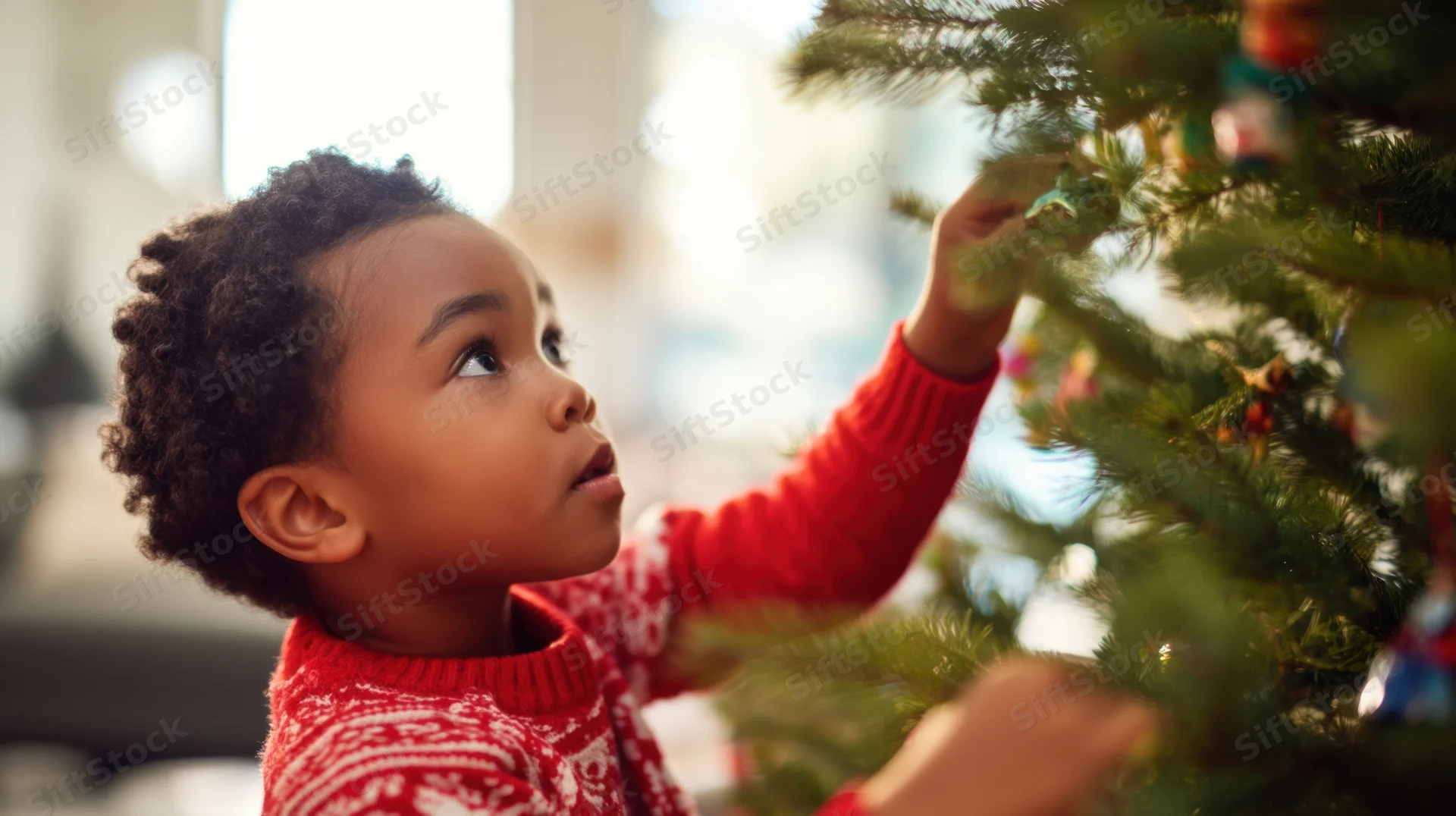 Young child decorating a christmas tree indoors wearing a red sweater
