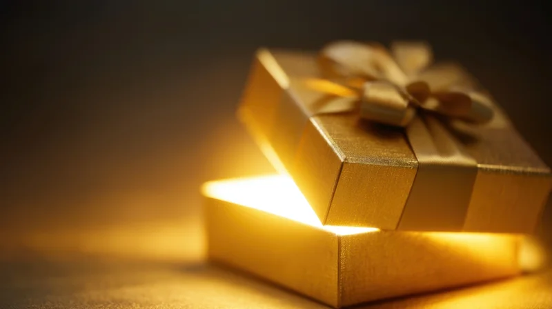 Golden gift box with glowing light inside, lid slightly open, on dark surface