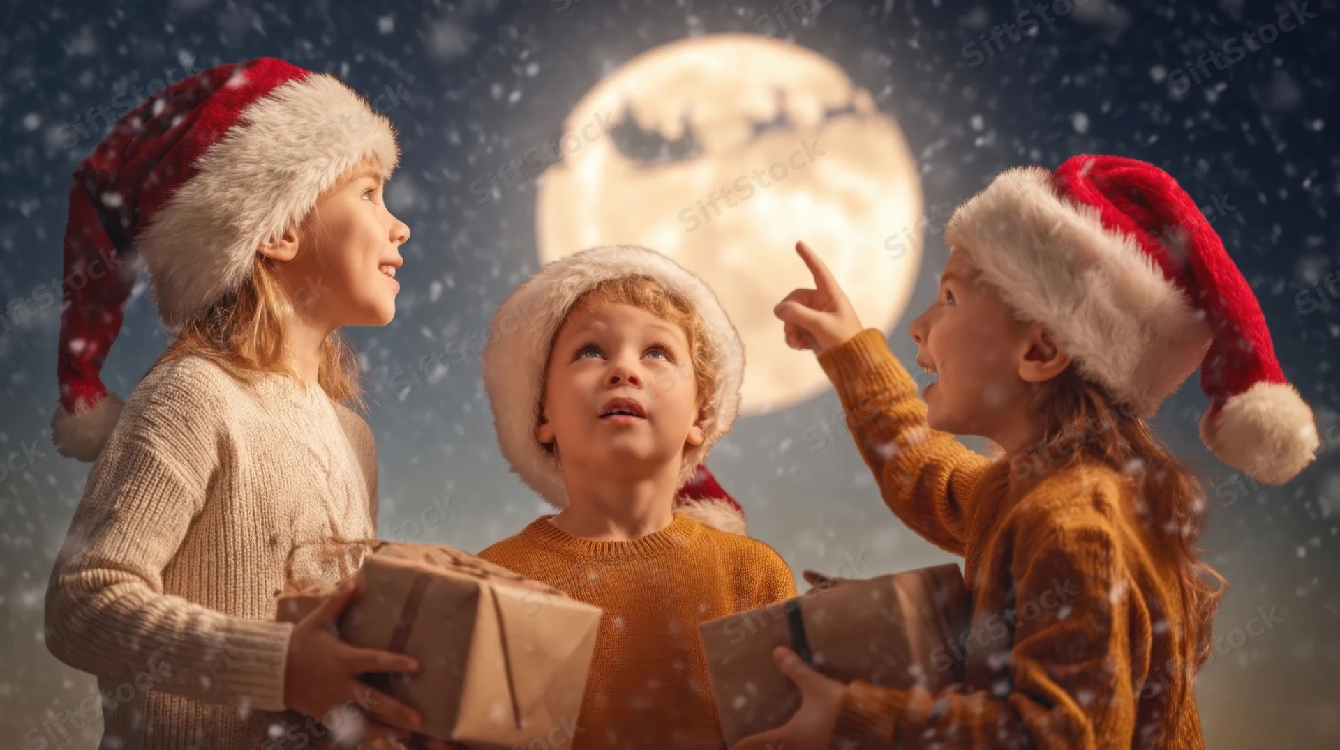 Three children in santa hats holding gifts and looking at a full moon with snow falling at night