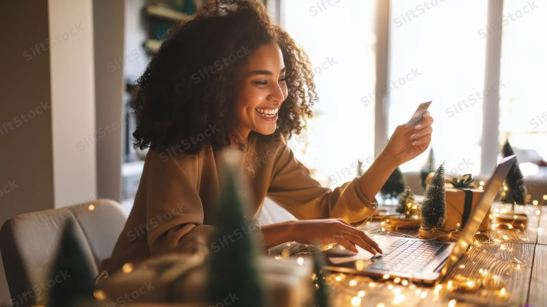 Young woman smiling while holding credit card and using laptop at decorated desk during christmas season
