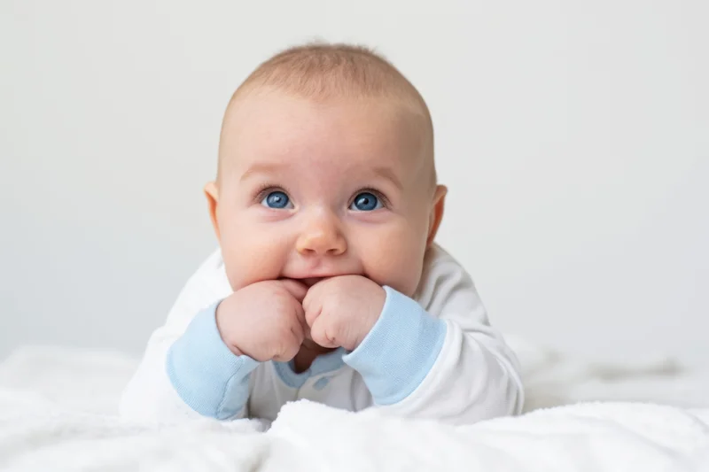 The baby lying on stomach with hands in mouth looking up adorably
