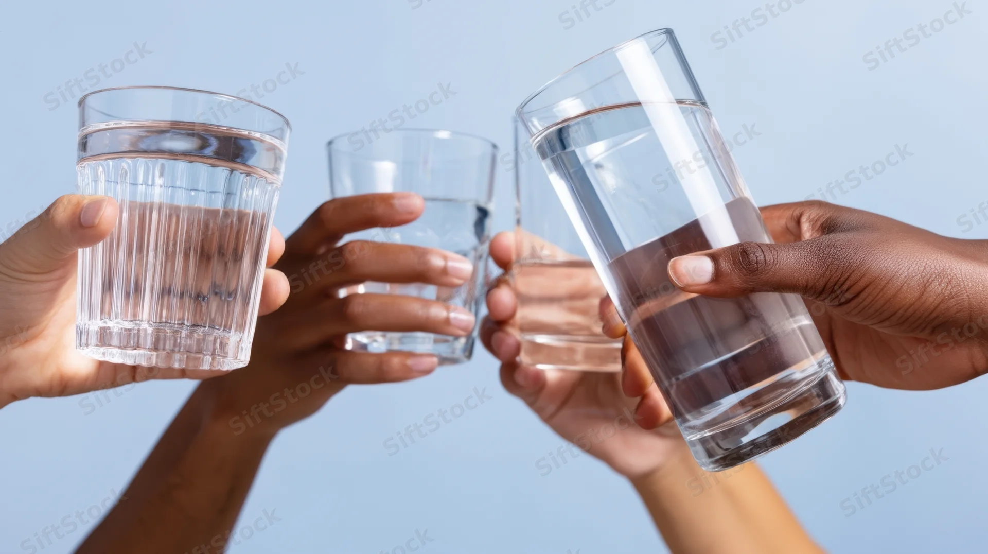 Hands holding glasses of water toasting against a light blue background