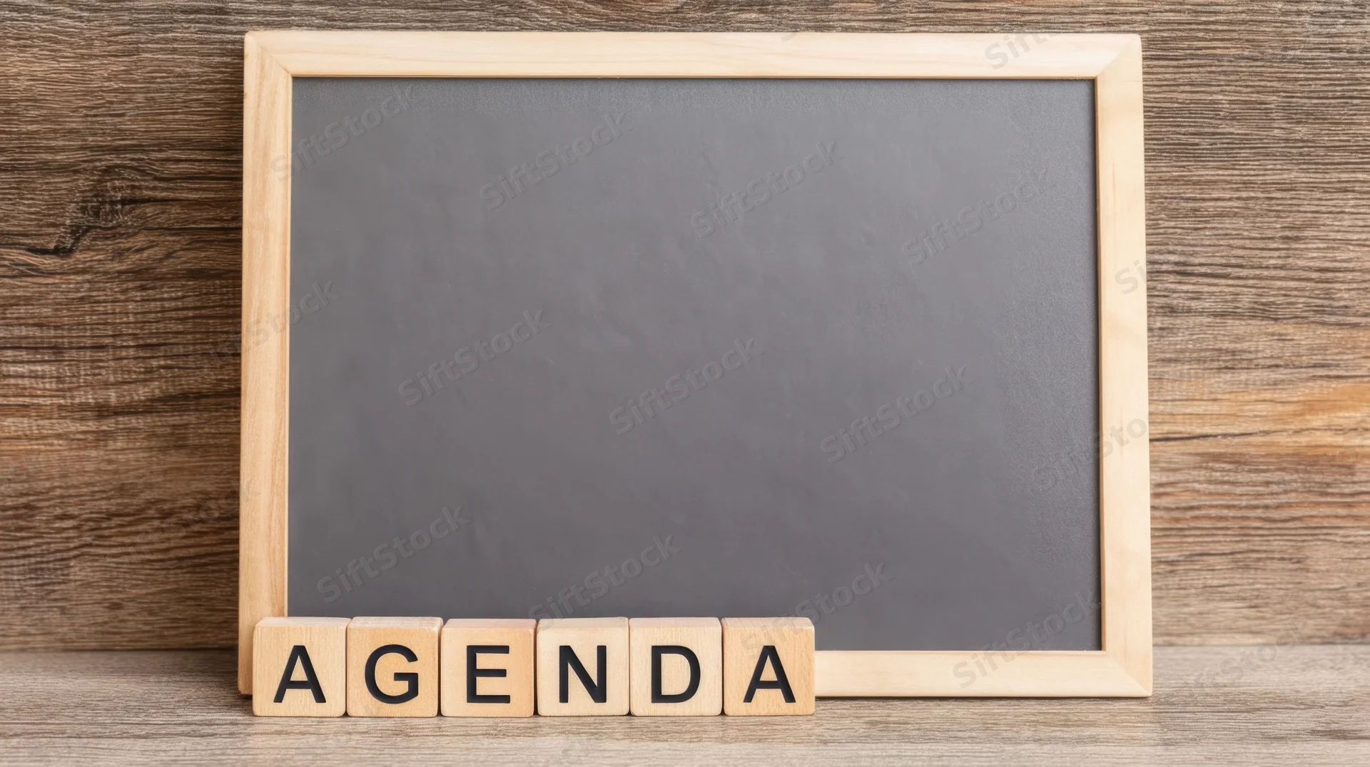 Wooden-framed chalkboard with wooden letter blocks spelling agenda on a wooden surface