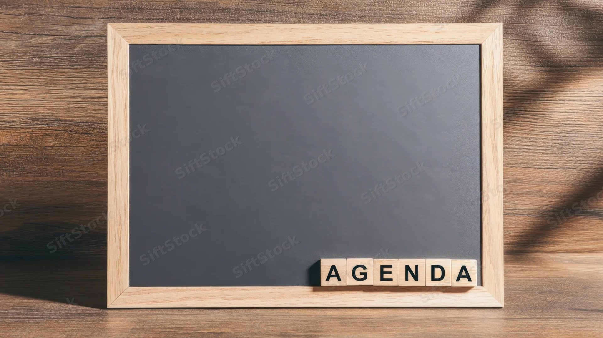 Wooden-framed chalkboard with wooden tiles spelling agenda on a wooden surface
