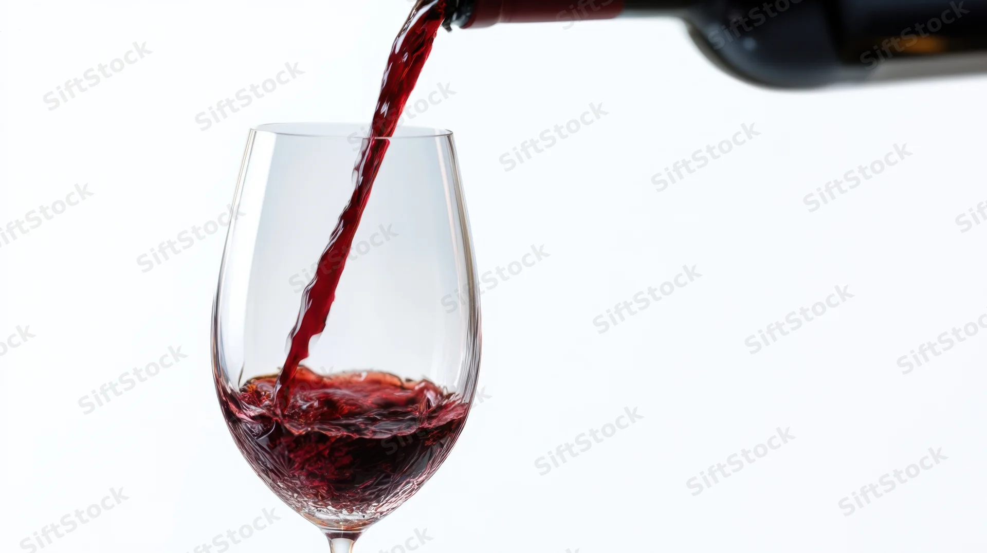 Red wine being poured from a bottle into a glass against a white background
