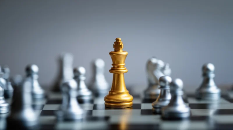 Golden chess king standing on board surrounded by silver pieces