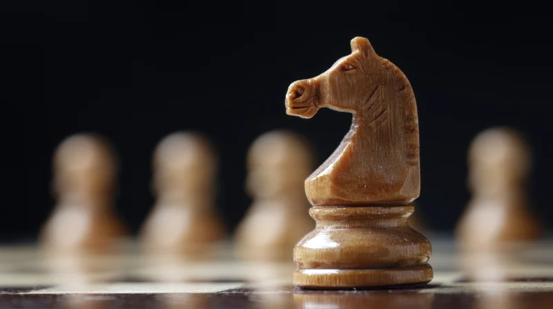 Wooden knight chess piece in focus on board with blurred pawns behind