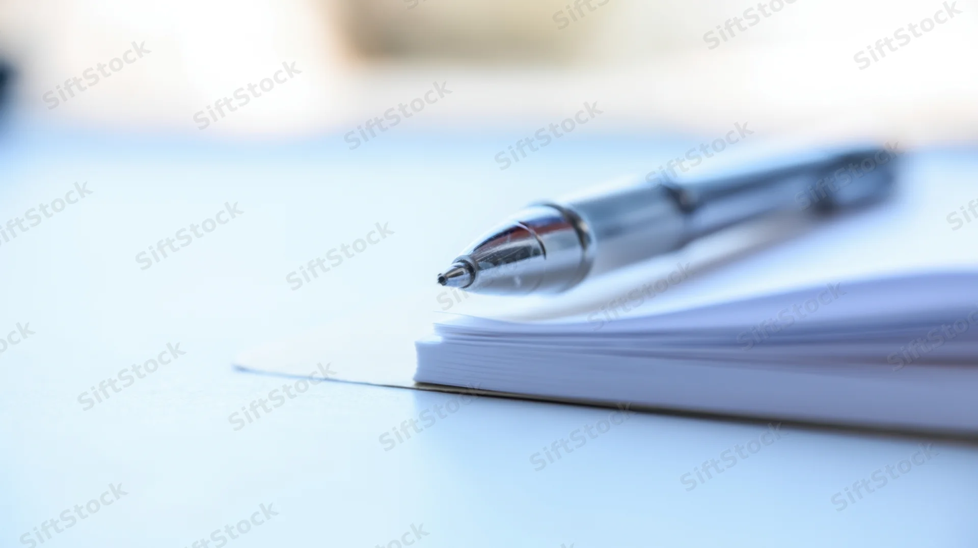 Silver pen resting on a stack of white notebook pages on a desk