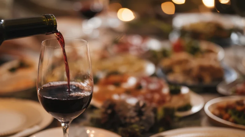 Red wine being poured into a glass at a festive dinner table with food and decorations