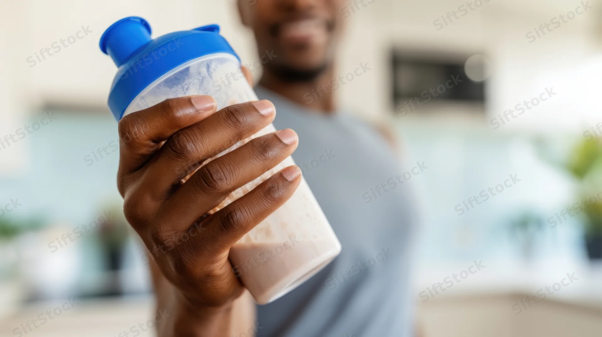 Man holding protein shake bottle in kitchen after workout