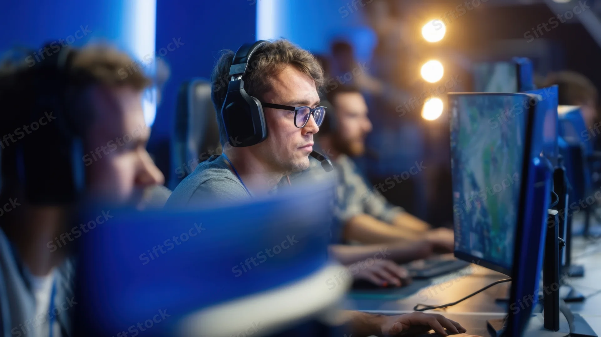 Gamer wearing headset and glasses focused on computer screen in esports arena