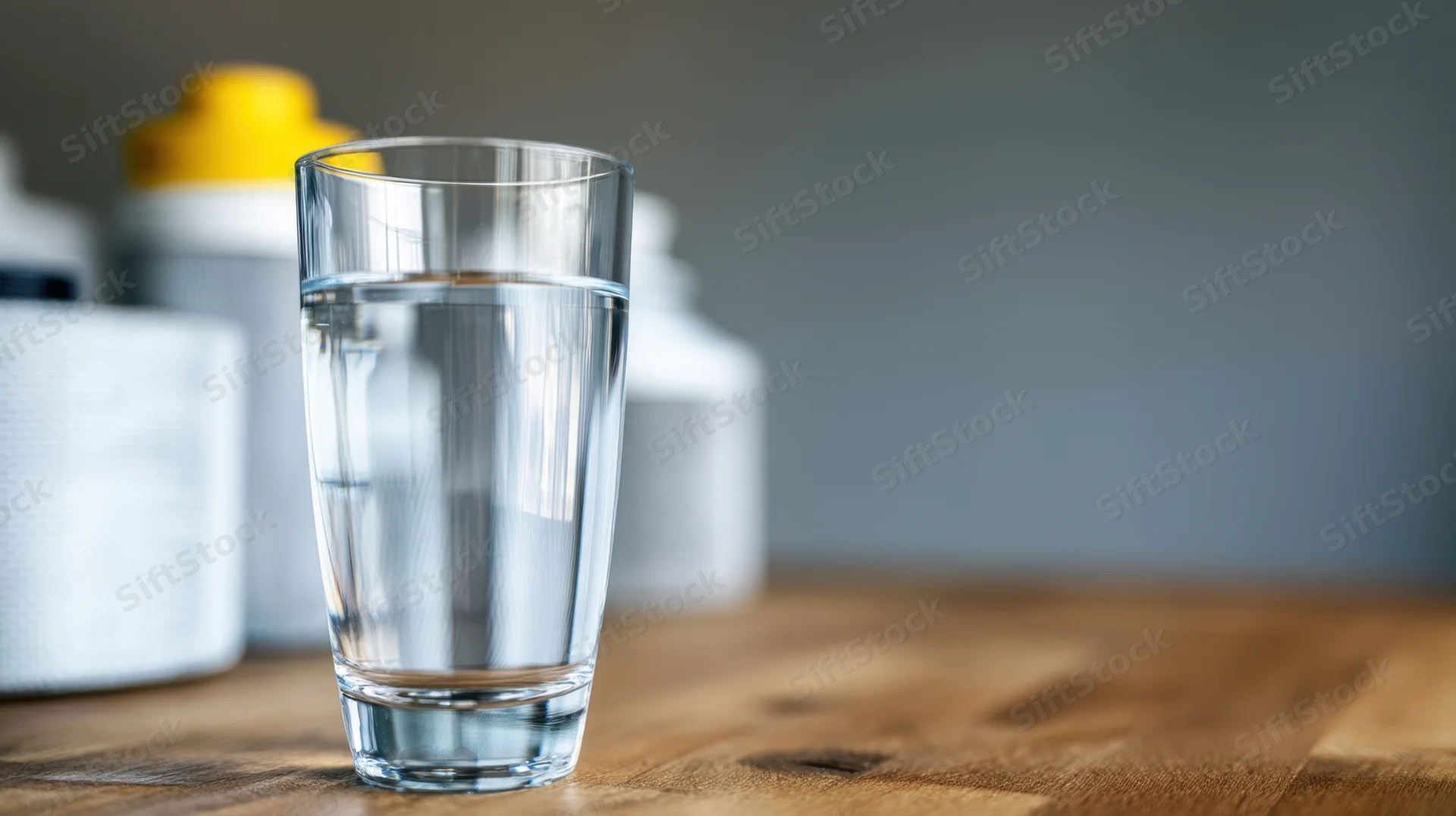 Glass of water on wooden table with bottles in background