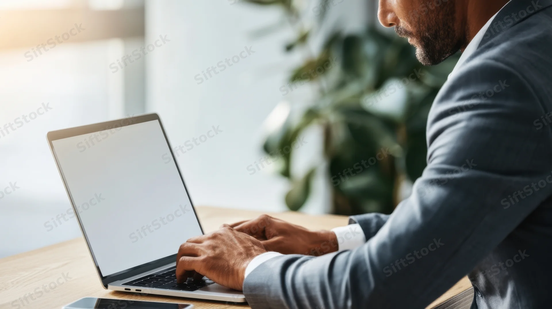 Man typing on laptop at office desk with plant in background