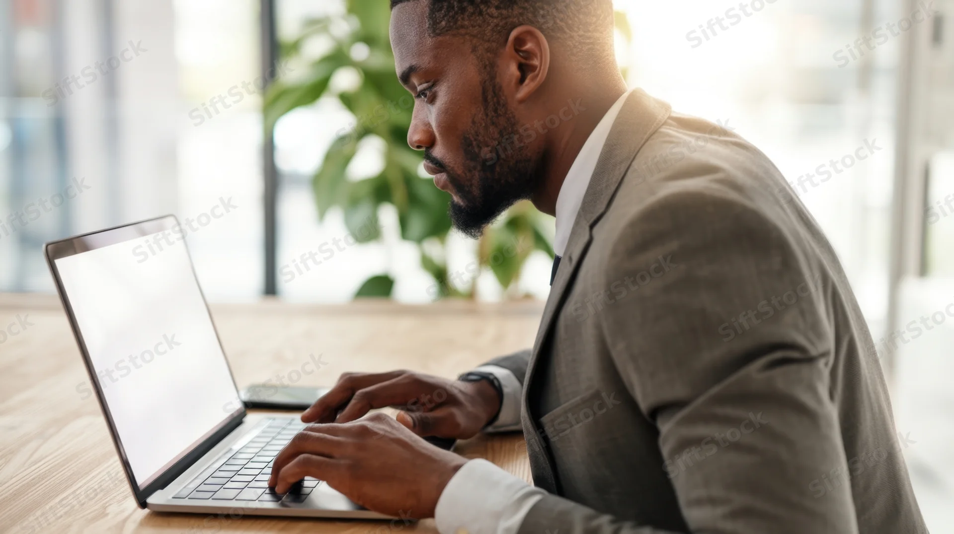 Man in suit typing on laptop at office desk near window