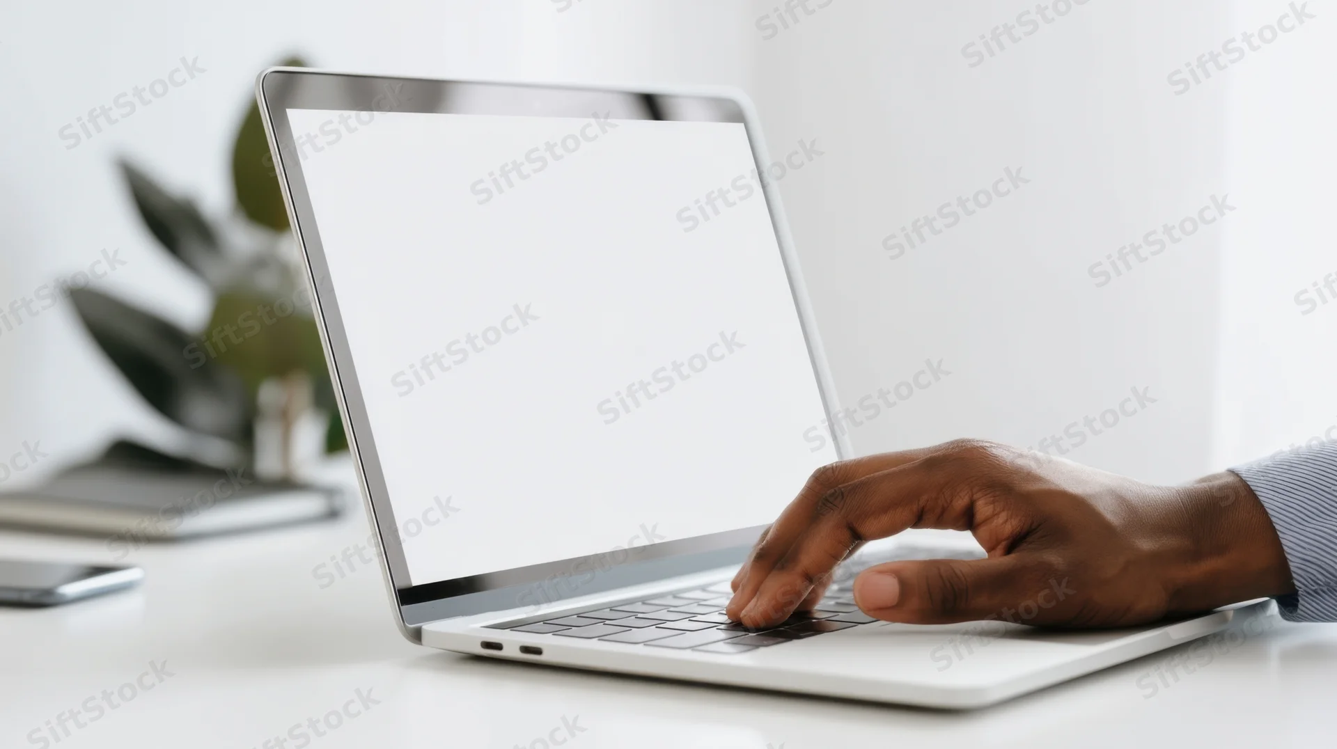 Hand typing on a laptop with blank screen on a white desk