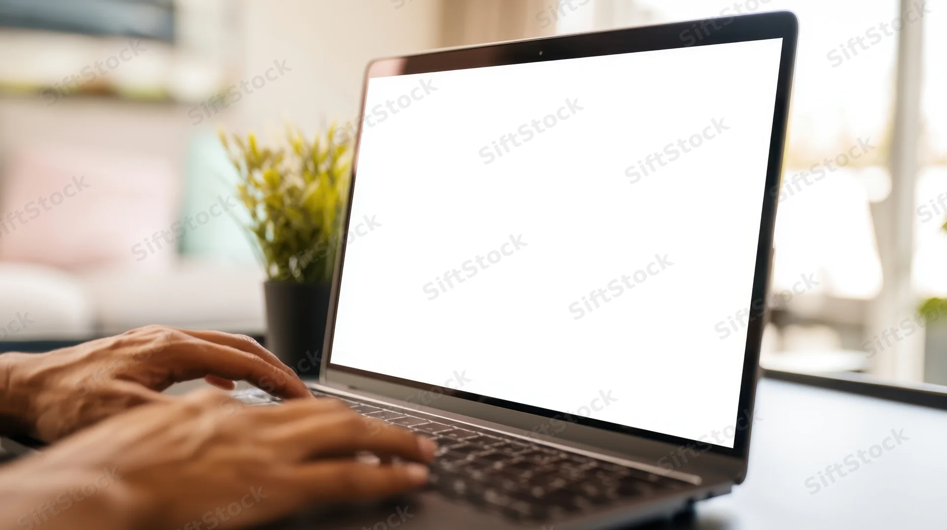 Hands typing on a laptop with blank white screen on a desk in a home office