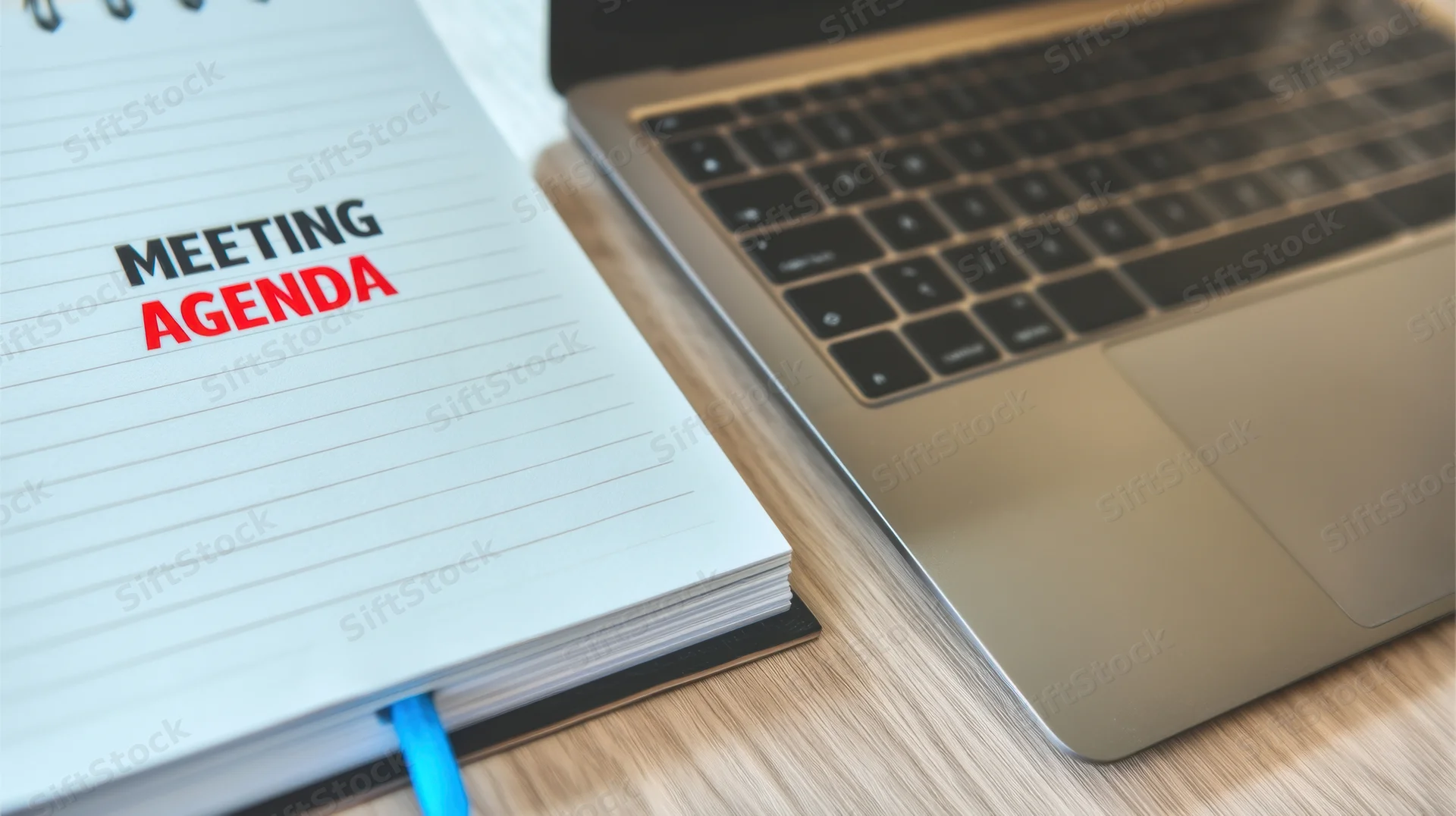 Notepad with meeting agenda text beside a laptop on a wooden desk