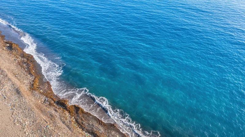 Polluted beach with plastic waste along the shoreline meeting turquoise ocean waves