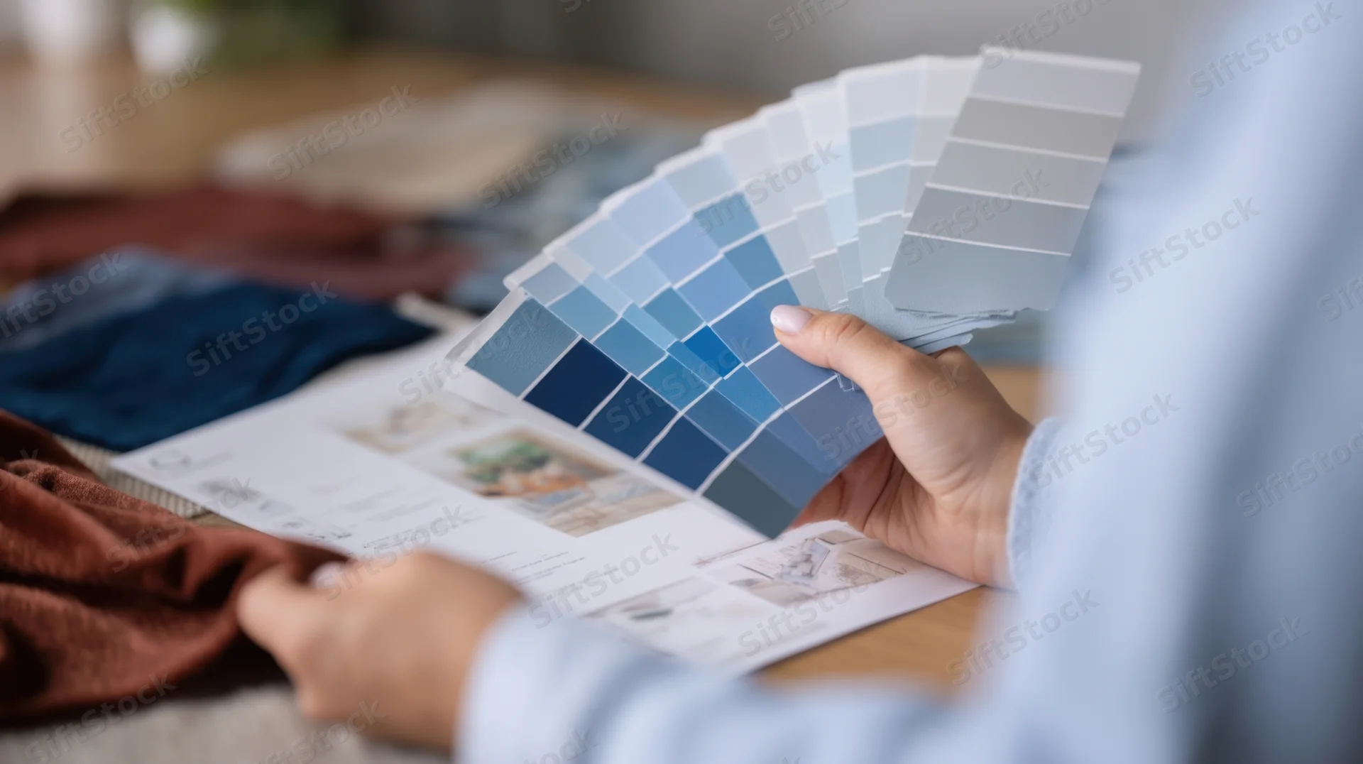Woman holding blue color swatches over fabric samples on desk for interior design planning