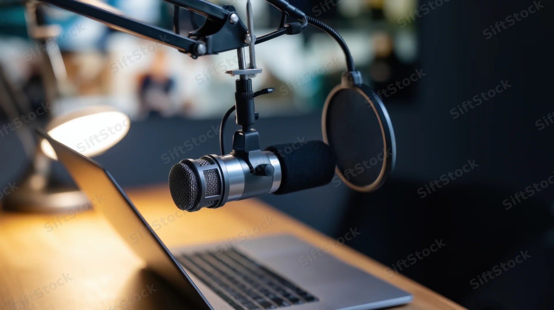 Professional microphone on boom arm with pop filter positioned over laptop on wooden desk in home studio setup