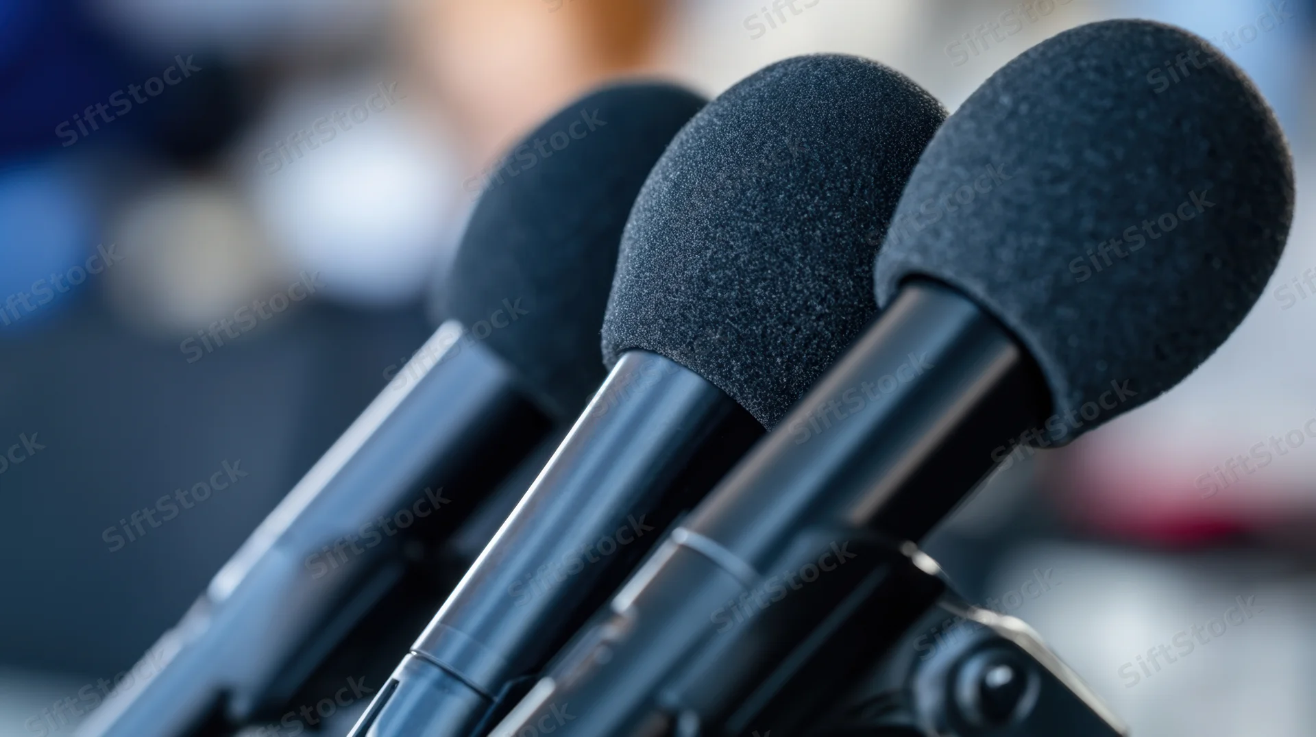 Three microphones with foam covers arranged in a row on a stand, ready for a press event