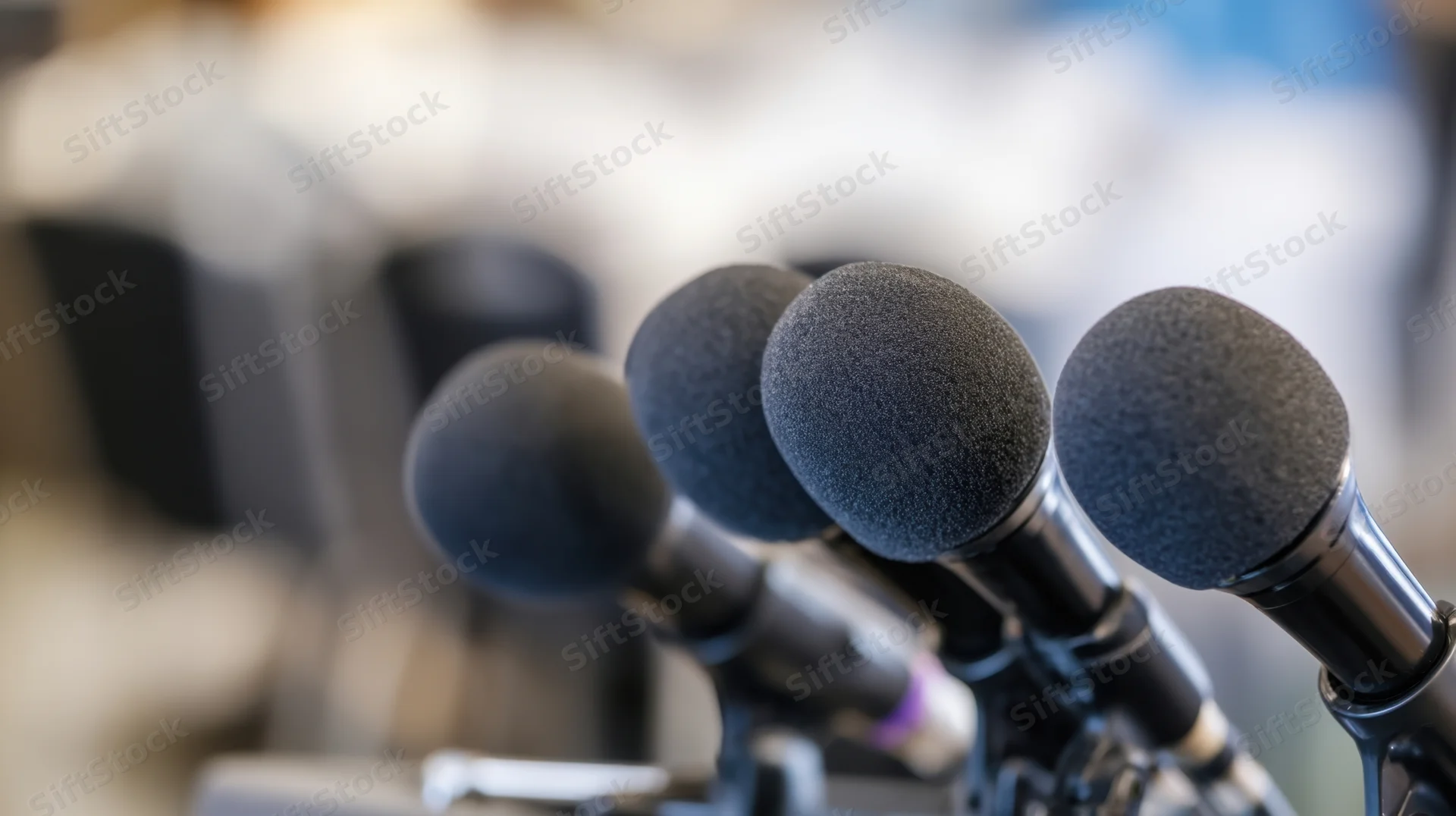 Row of microphones with foam covers on stands at a press event