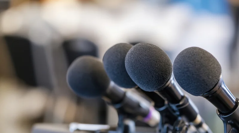 Row of microphones with foam covers on stands at a press event